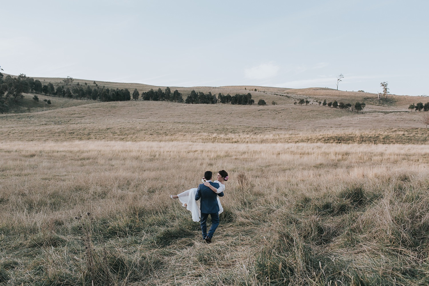 groom carries his bride into the fields at bendooley estate