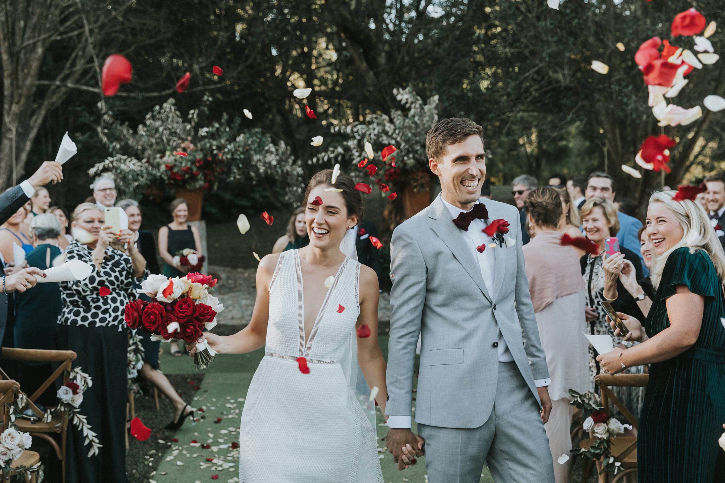 massive smiles from the bride and groom as guests throw rose petals at them